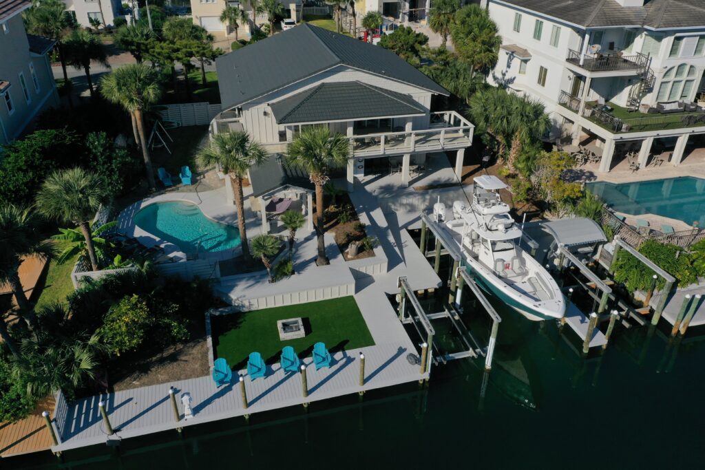 Aerial view of a waterfront home with a boat dock, pool, and WortHouse roof.
